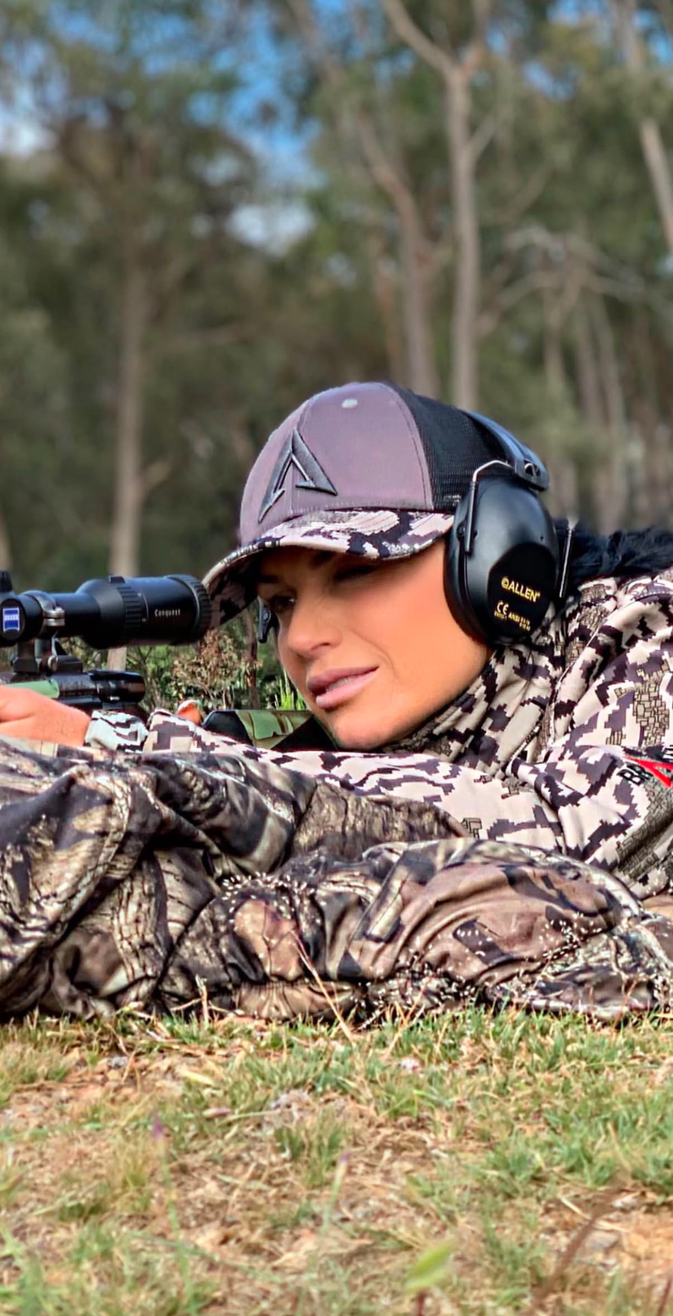 Sharelle Galea lying prone in camo behind her rifle, glassing across the paddock