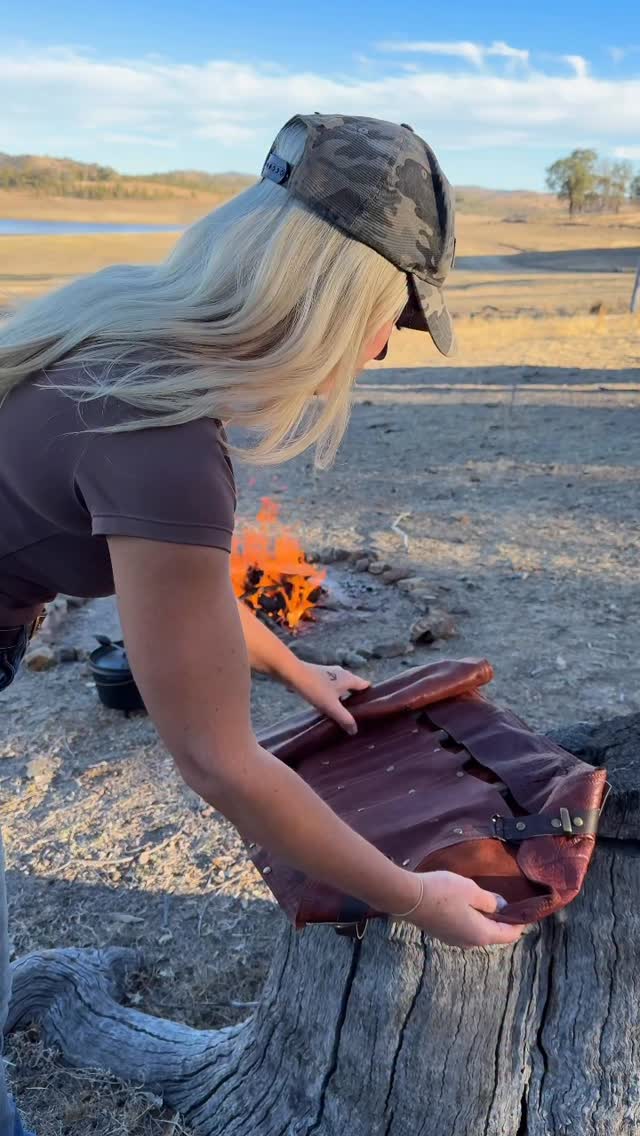 Emma by the campfire at golden hour, unrolling a leather knife roll