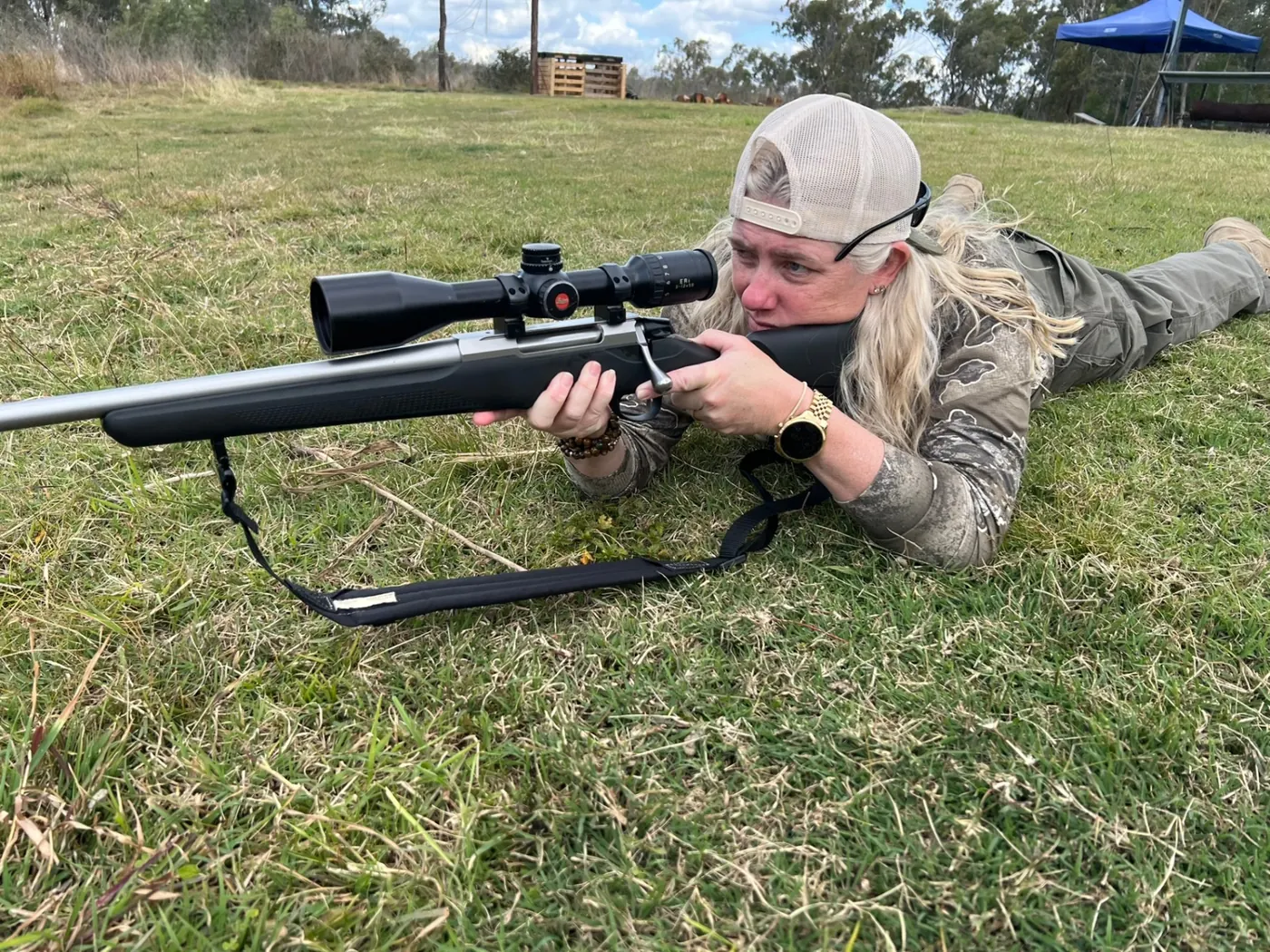 Carly lying prone in the grass, sighting through a rifle scope at the range