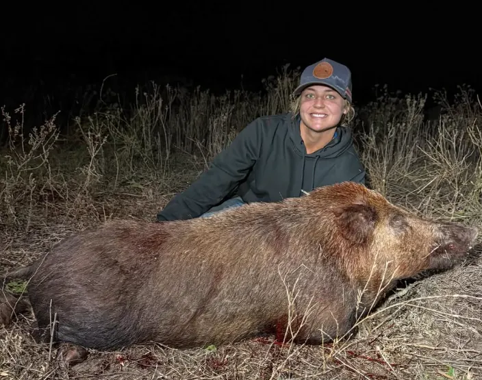 Taylor smiling behind a large feral pig in long grass